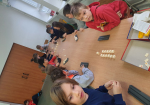 Dzieci siedzą przy stołach i grają w grę planszową.