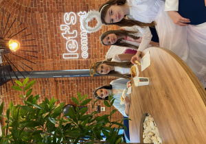 4 dziewczynki, przebrane za anioły siedzą przy stole i jedzą pyszne bułeczki.