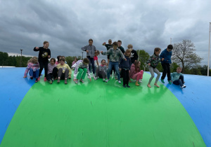 chłopcy i dziewczynki siedzą lub stoją na ogromnym, zielono-niebieskim balonie