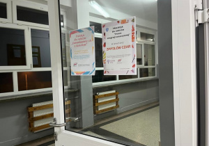 Drzwi sali lekcyjnej, na których wiszą plakaty informacyjne o spotkaniu specjalisty z rodzicami.