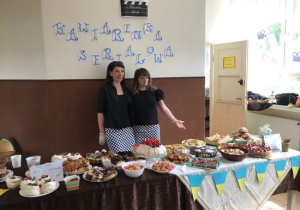 Dwie kobiety stoją za stołem z ciastami i innymi słodkościami