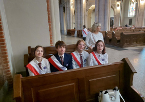 Uczniowie ubrani na galowo siedzą w ławce w kościele