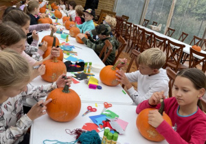 dzieci siedzą przy długim stole i ozdabiają dynie