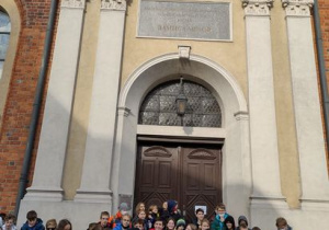 Uczniowie z klas siódmych i ósmych stoją przed dużym żółtym budynkiem.
